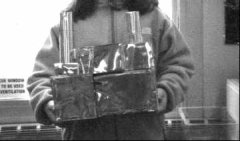 Child holding tin foil building.