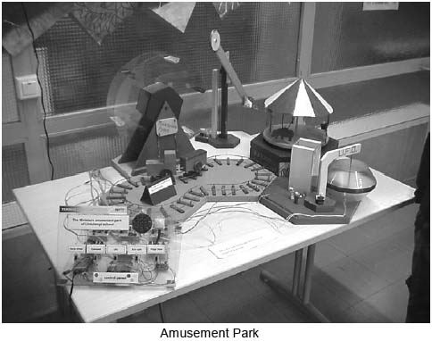 A photograph of an amusement park created using the project boards. It includes projects such as the ferris wheel, the sun spin, a train ride, a merry-go-round and a UFO ride.  The project board controlling the amusment park is featured on the table with all the rides in the front-left corner.