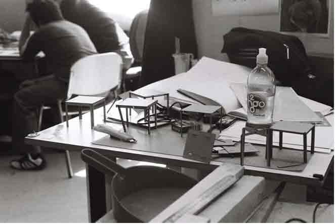 Table full of Papers, notebook, small table-like models and a water bottle.