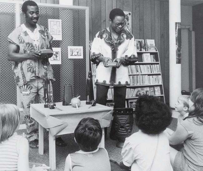 Two African-American men in ethnic dress present to group of children.